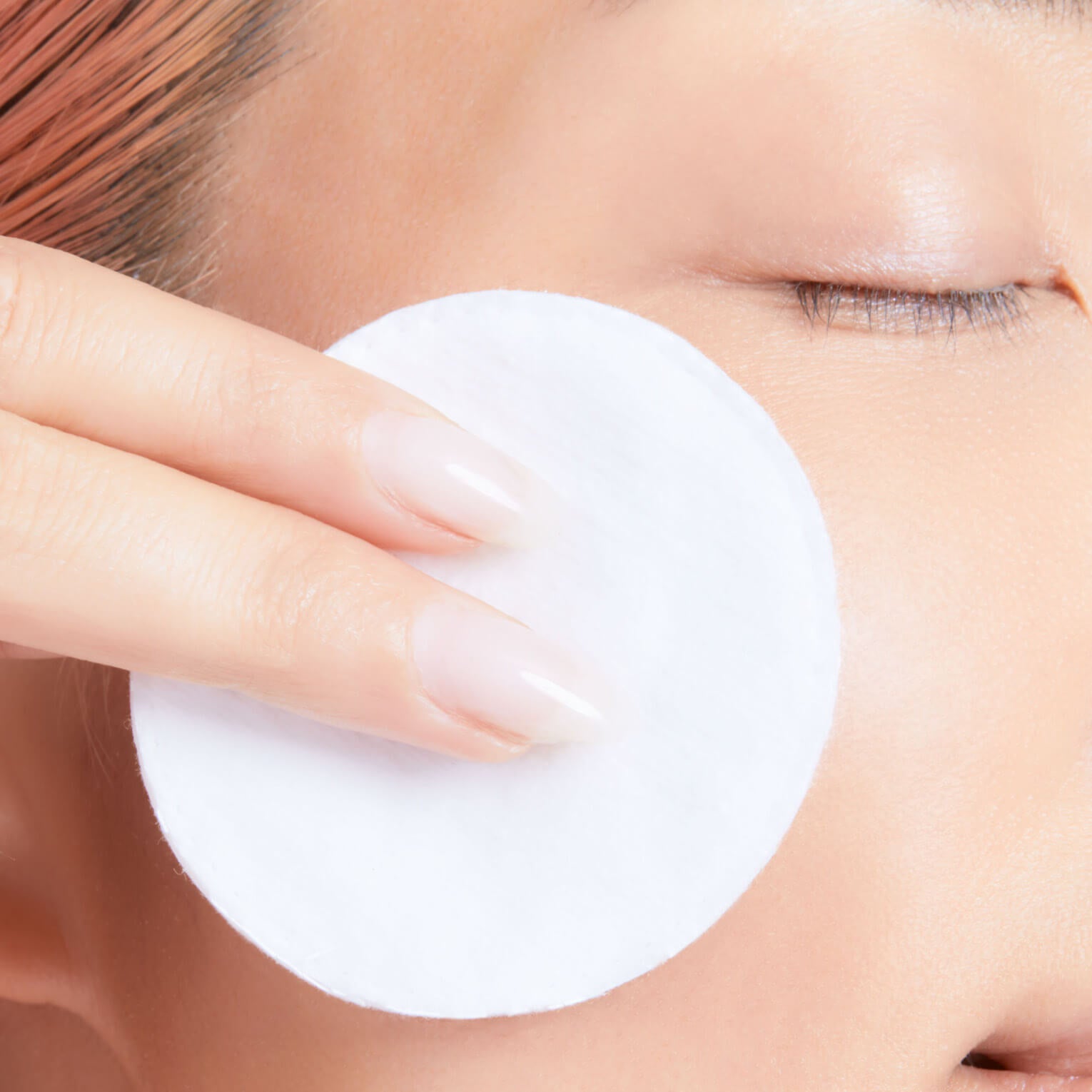 Person applying active tonic to their face with a cotton swab