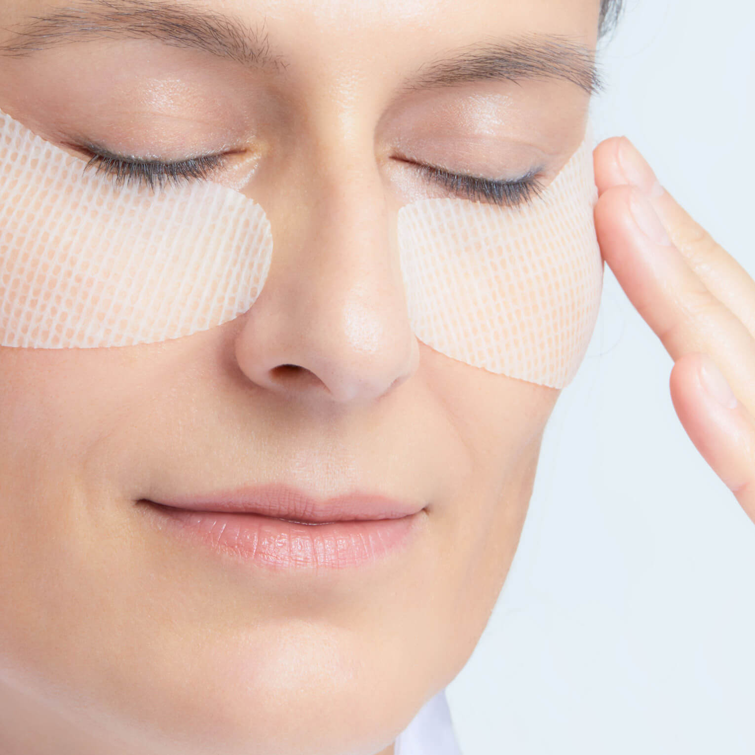 Woman applying eye patches to her face with a neutral background