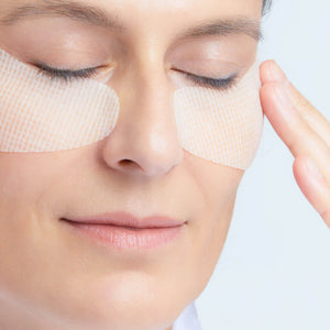 Woman applying eye patches to her face with a neutral background