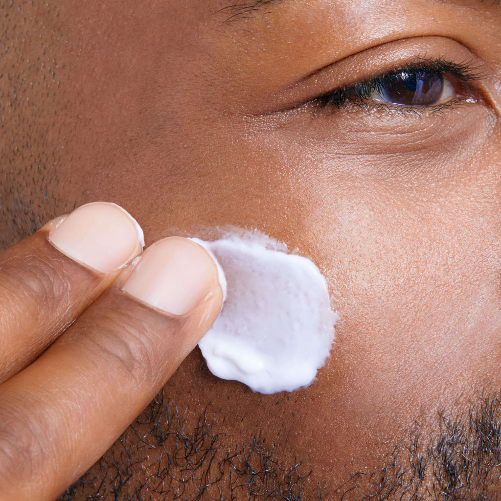 Man applying cream to his face with a close-up view of his eye.