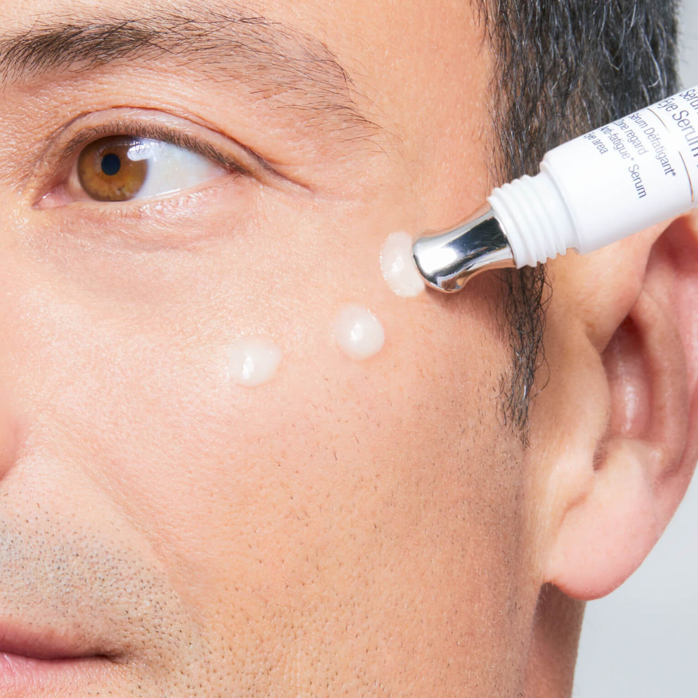 Close-up of a man applying cream to his face with a small applicator.