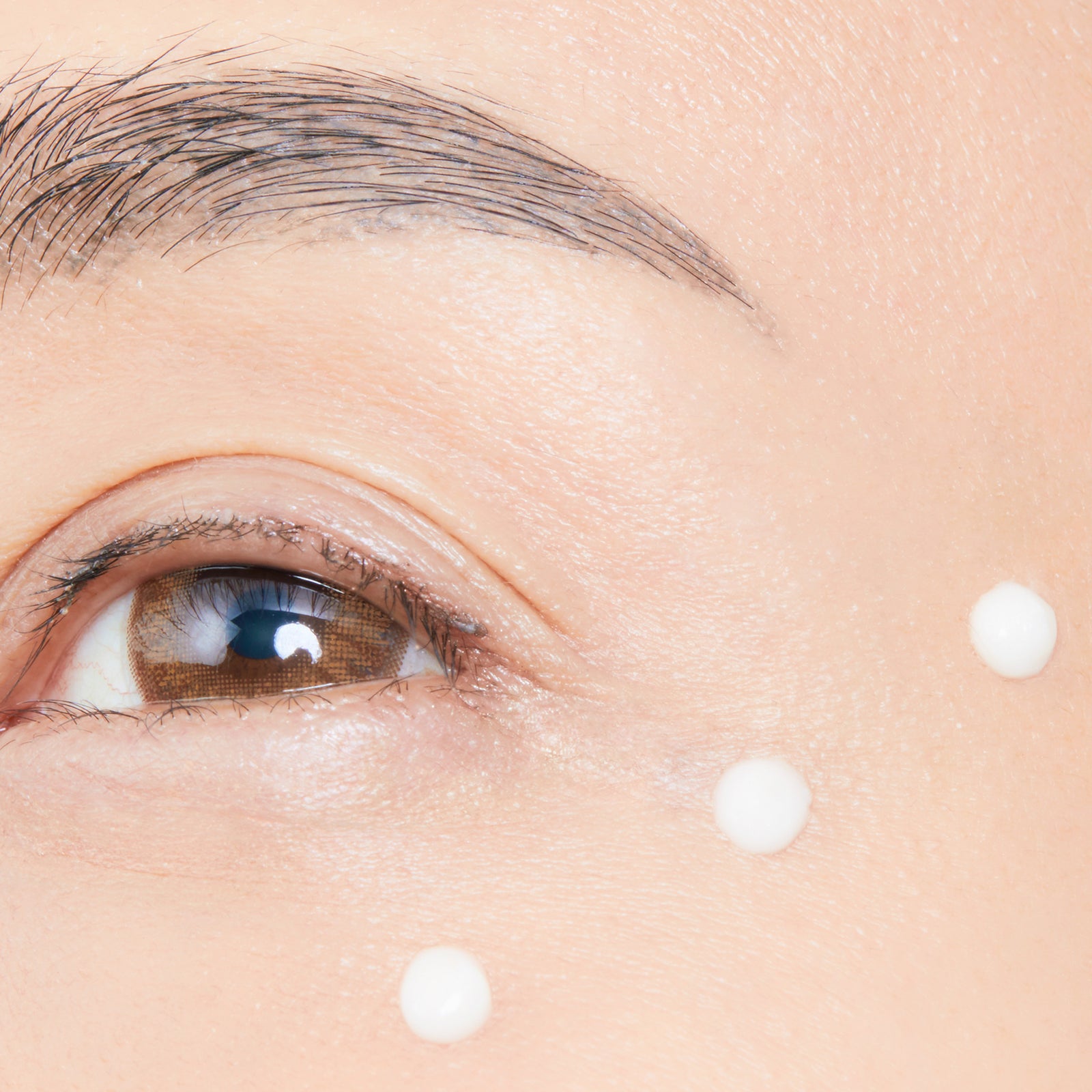 A close-up of a woman's eye area featuring with white dots, showcasing the application of Cellular Eye Contour Cream.