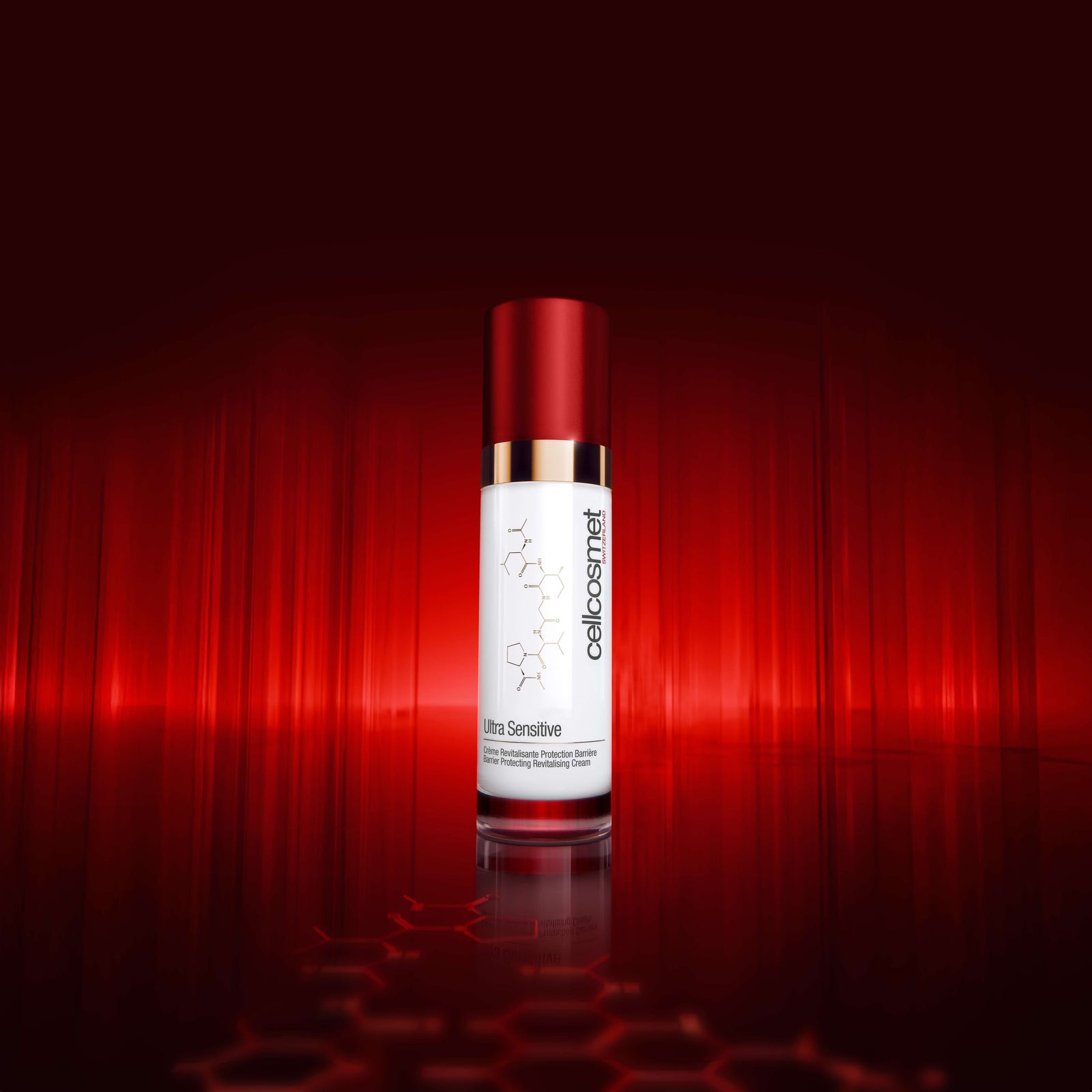 A bottle of Cellcosmet Ultra Sensitive Face Cream, featuring a white bottle with a metallic red cap and gold collar, set against a dramatic red studio background with a reflective surface.