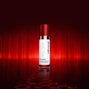 A bottle of Cellcosmet Ultra Sensitive Face Cream, featuring a white bottle with a metallic red cap and gold collar, set against a dramatic red studio background with a reflective surface.