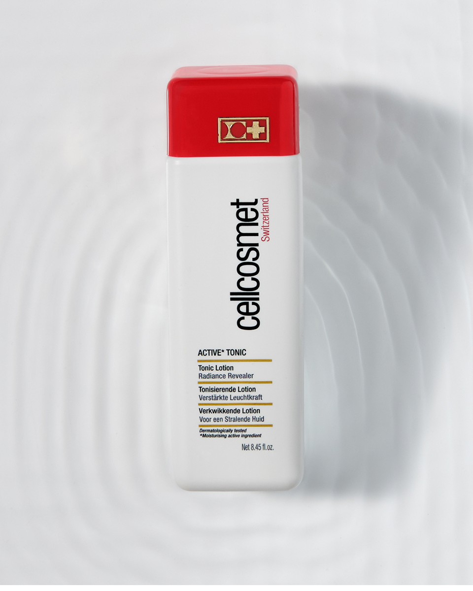 Cosmetic bottle of active tonic with red cap and white body on a light gray background