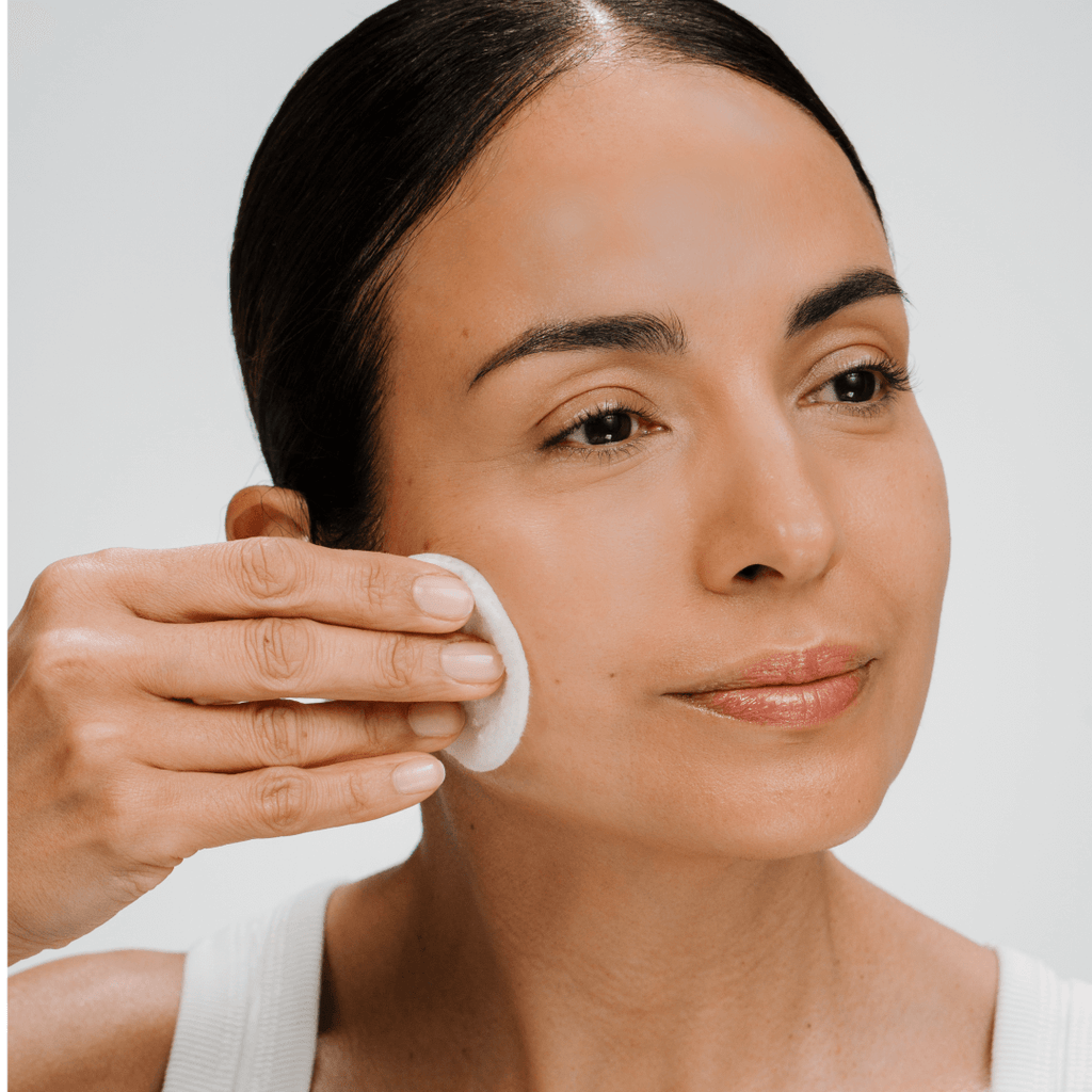 Woman applying a active tonic with a cotton pad on a plain background
