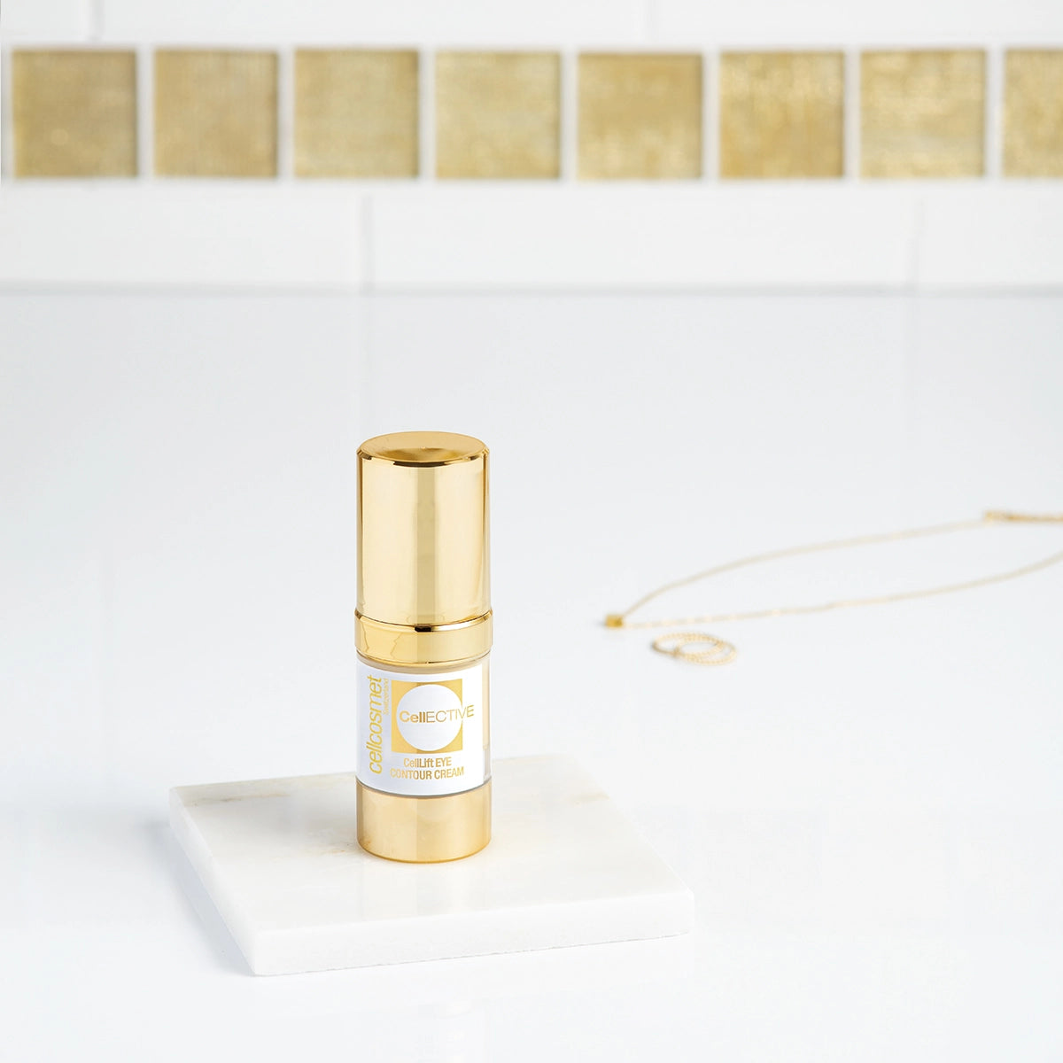 CellLift Eye Contour Cream, a gold and white bottle, displayed on a white marble countertop with jewelry in the backdrop.