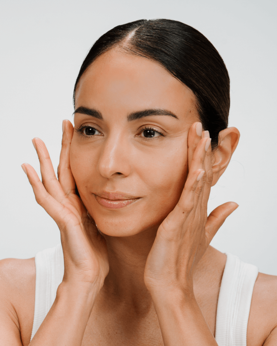 Woman messaging cream into her face with a neutral background