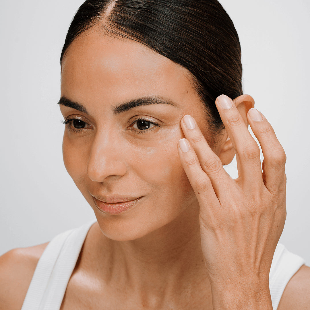 Woman applying CellLift Eye Contour Cream skincare product to her face with a neutral background