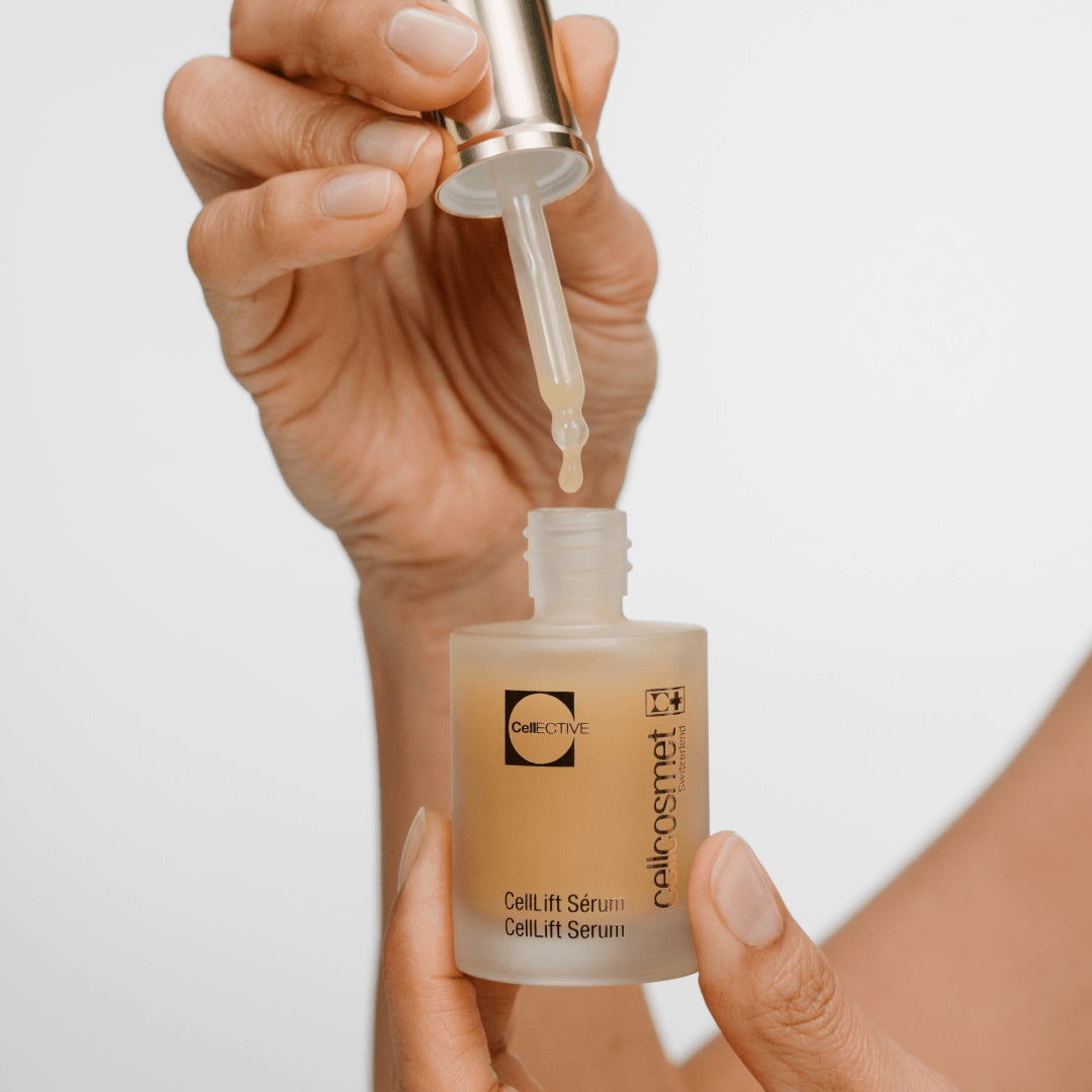 Hand holding a dropper over a bottle of CellLift Serum by cellecosmet against a light background