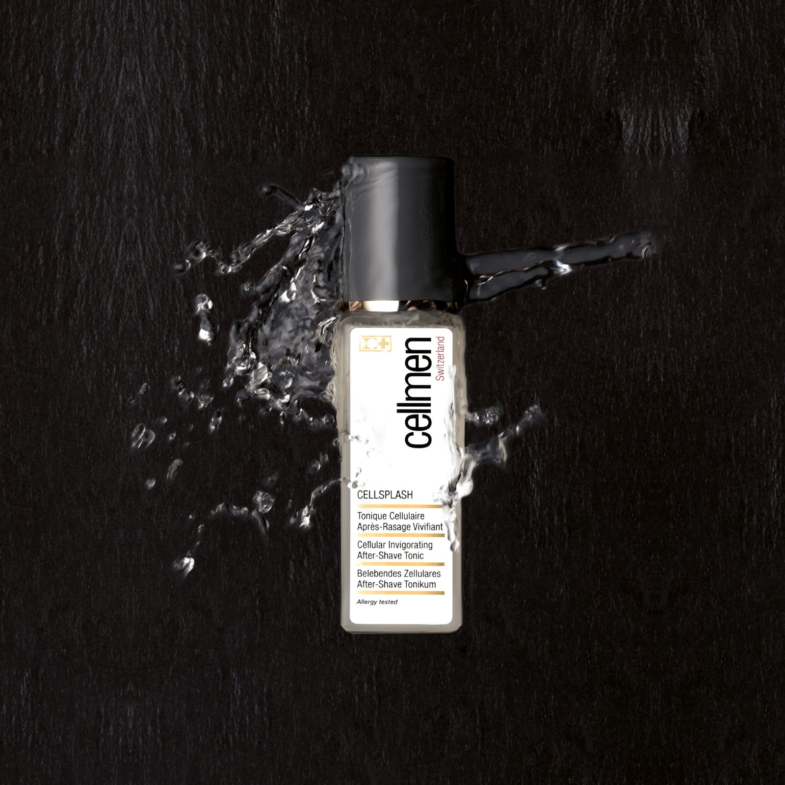 A bottle of Cellmen Cellsplash skin care product on a black surface, surrounded by splashes of water for a refreshing effect.