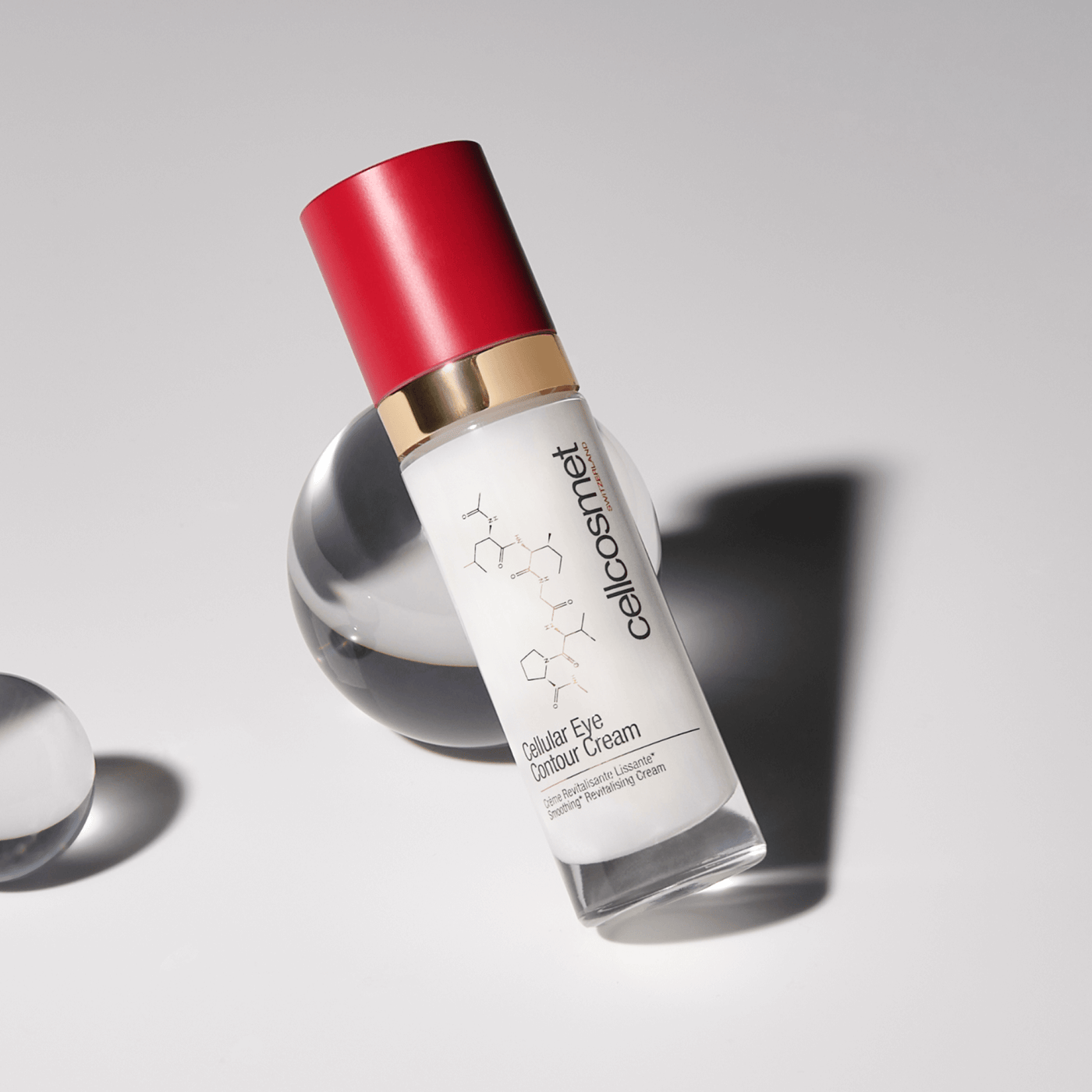 Skincare bottle of cellular eye contour cream with red cap and white label on a gray background