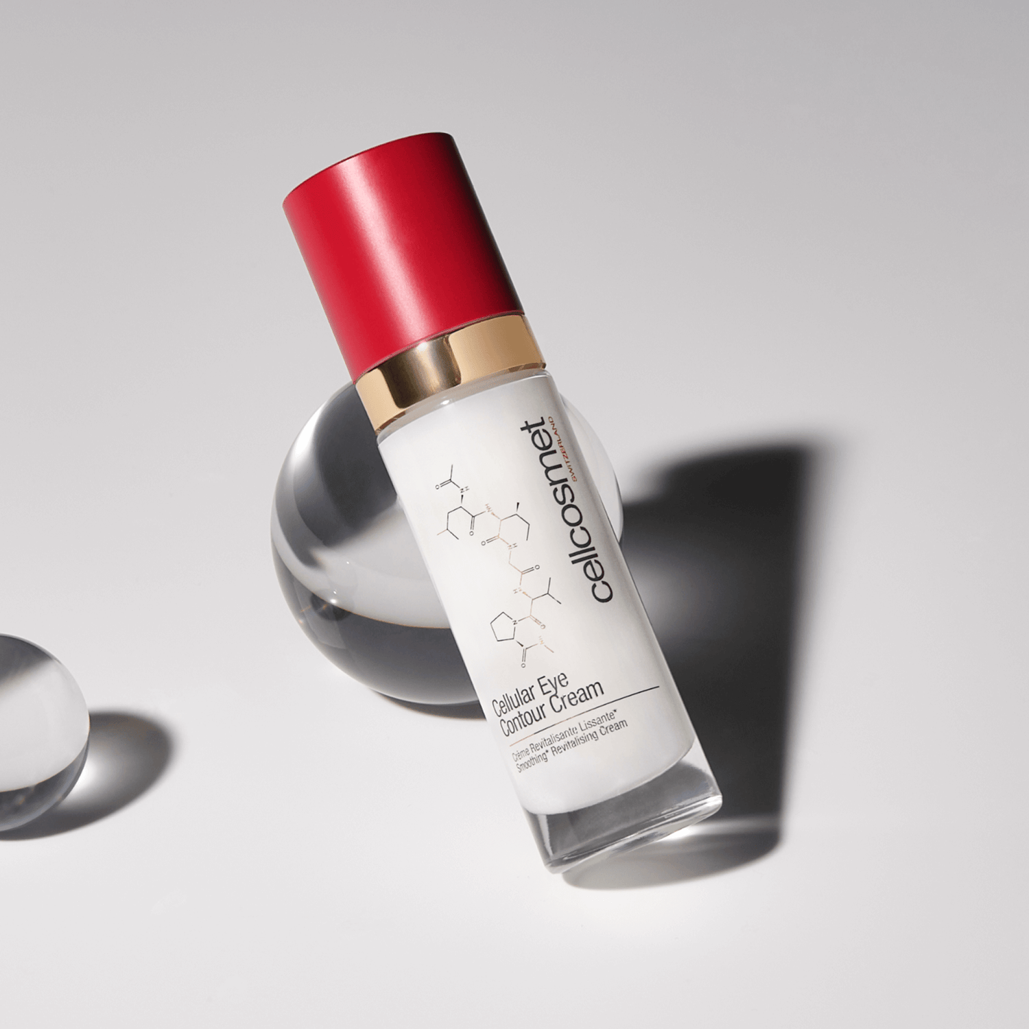 Skincare bottle of cellular eye contour cream with red cap and white label on a gray background