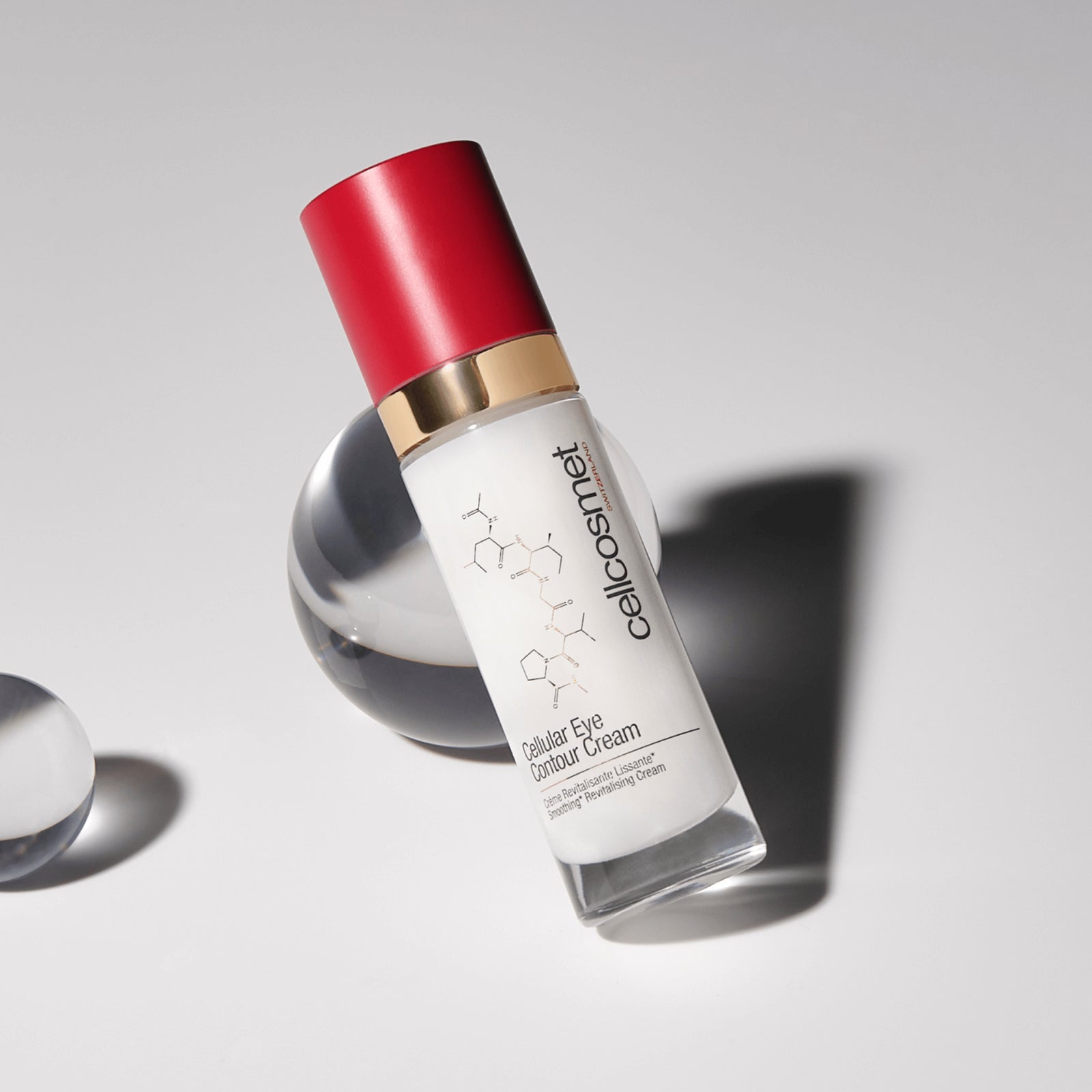 Skincare bottle of cellular eye contour cream with red cap and white label on a gray background