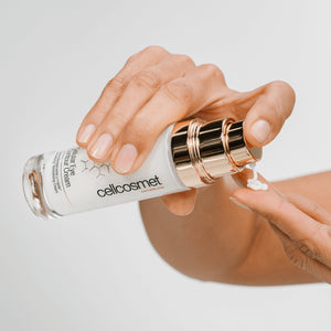 Hand applying cellular eye controur cream from a cellcosmet bottle on a light background