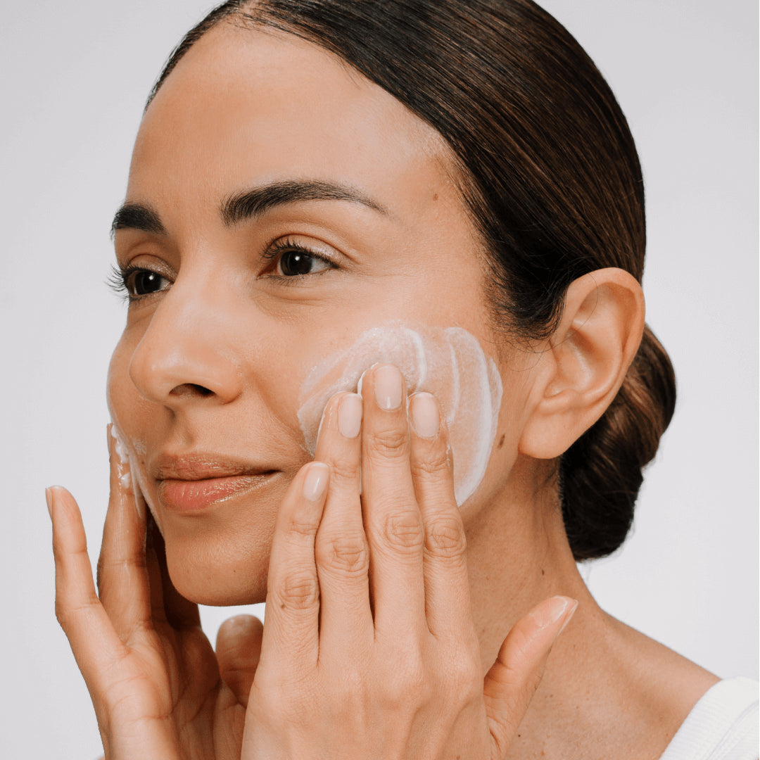 Woman applying a skincare product to her face with a neutral background