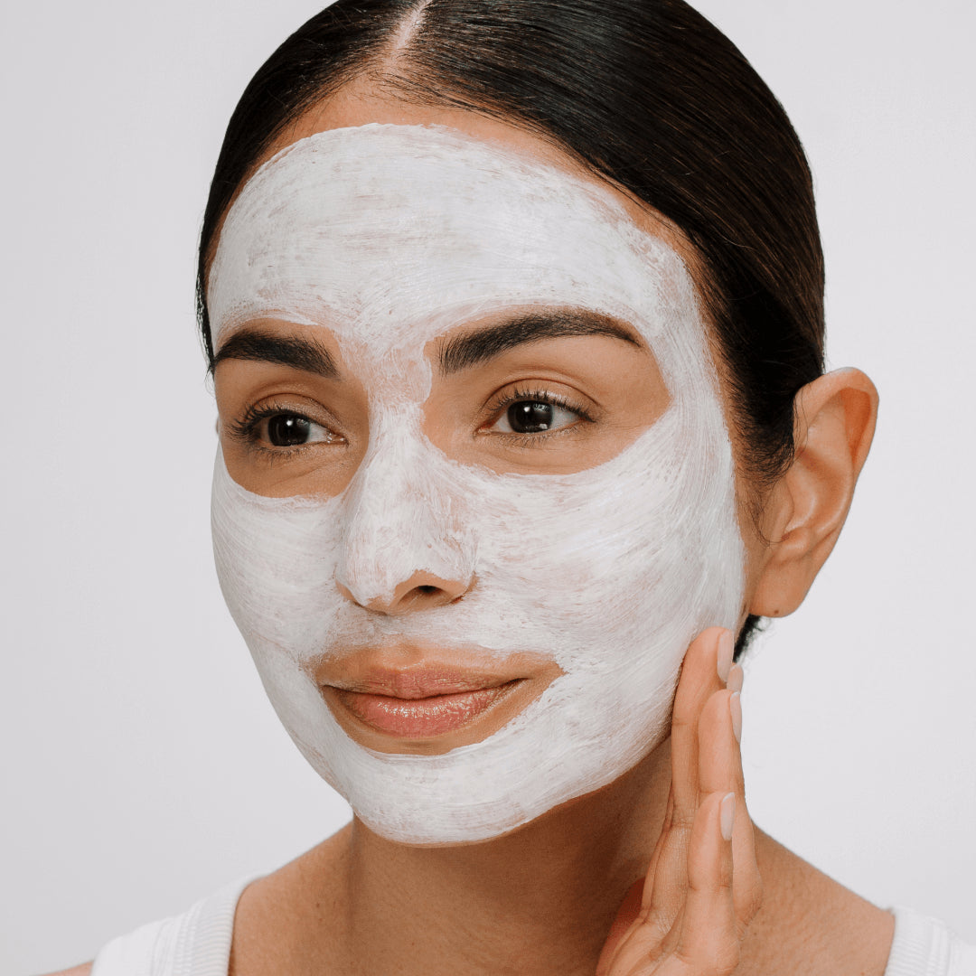 Woman applying a hydra soothing facial mask on a plain background