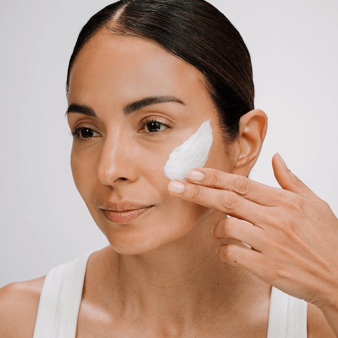 Woman applying hydra soothing mask to her face with a neutral background