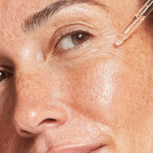 Close-up of a woman's eye with a dropper applying a substance to her skin.