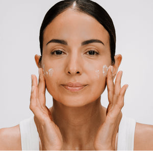 Woman applying ultra vital cream to her face with a plain background